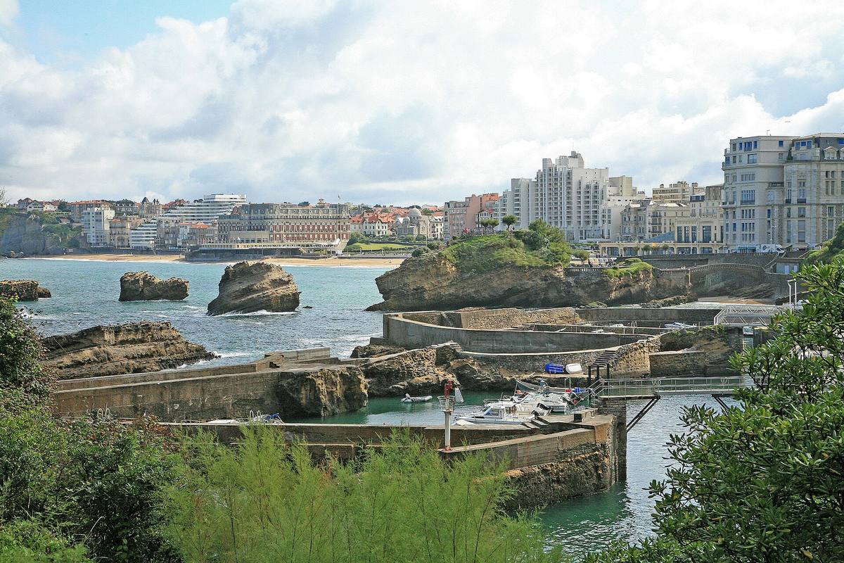 Le port des Pêcheurs de Biarritz entre les rochers, avec la Grande Plage et l'Hôtel du Palais en arrière-plan