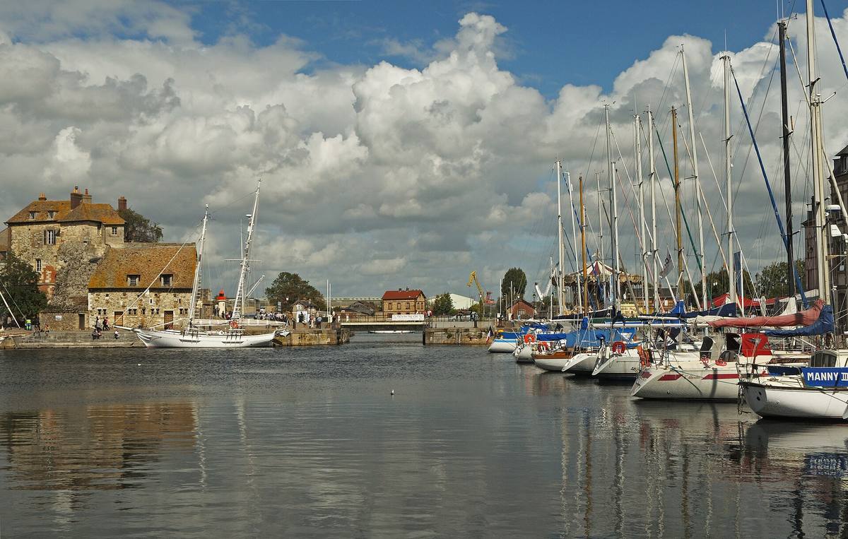Le Vieux Bassin de Honfleur avec ses voiliers amarrés et la Lieutenance en pierre à l'entrée du port, sous un ciel nuageux