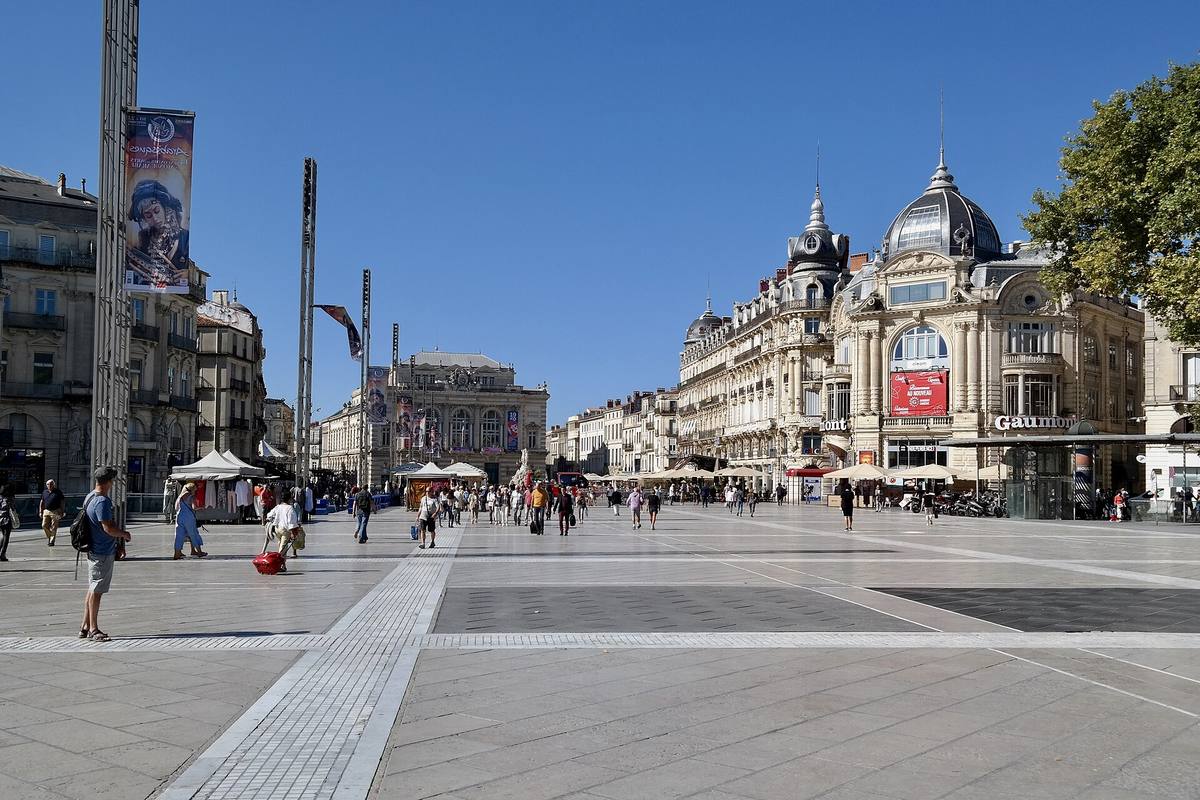 La place de la Comédie à Montpellier, vaste esplanade dallée bordée d'immeubles à dômes et de l'Opéra Comédie au fond