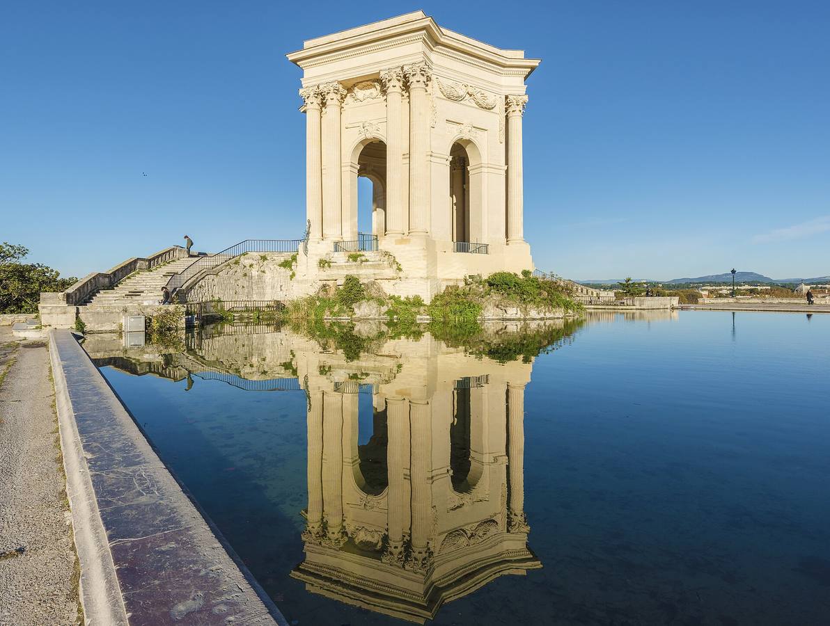 Le château d'eau à colonnes de la promenade du Peyrou à Montpellier, reflété dans son bassin sous un ciel bleu